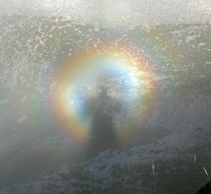 Shadow surrounded by a colorful light halo seen through misty fog on a snowy mountain, an alternate angle in history moments.