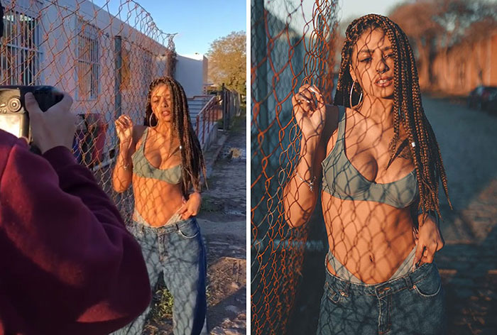 Photographer capturing behind the scenes of a model posing by a chain-link fence in natural outdoor lighting.
