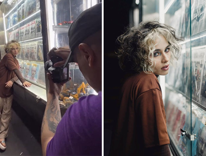 Photographer capturing behind the scenes moments with model posing by a glass display in a dimly lit setting.