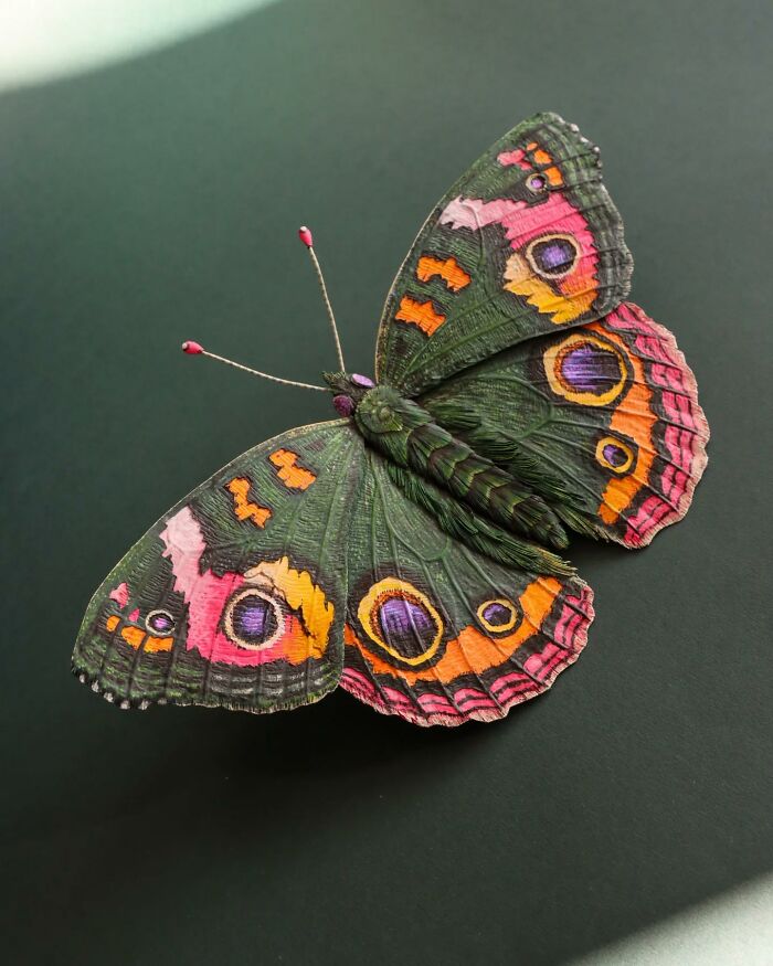 Lifelike paper and wood butterfly crafted by artist, showcasing detailed textures and vibrant colors on dark background.