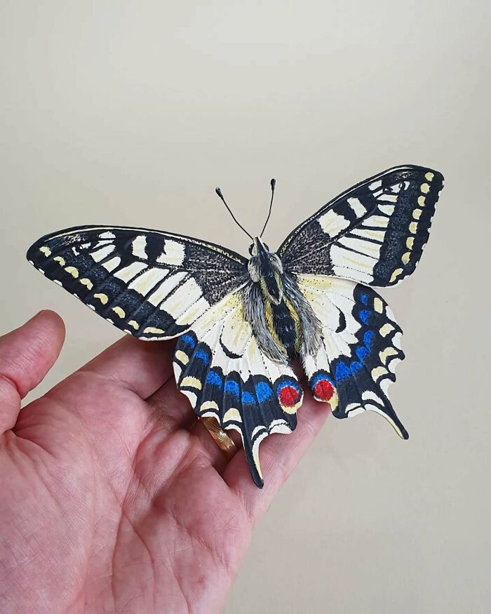 Hand holding a lifelike butterfly crafted from paper and wood, showcasing detailed and realistic bird art.