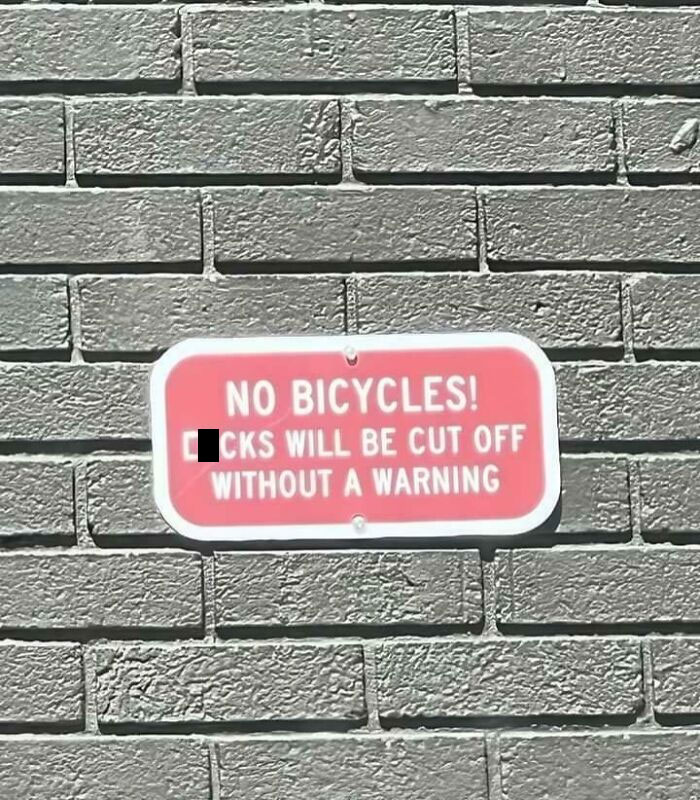 Red sign on brick wall warning no bicycles allowed, showcasing wholesome vandalism improving streets and public spaces.