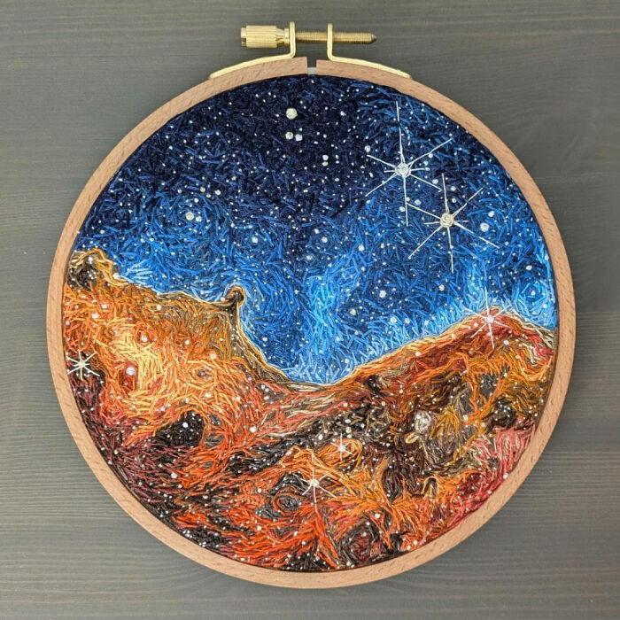 Embroidery hoop with a detailed stitch design of a starry night sky over rocky terrain showcasing beautiful embroidery designs.