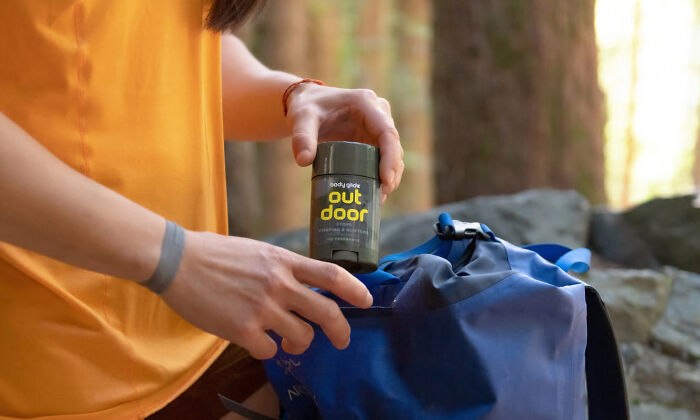 Person in an orange shirt holding a small outdoor item, packing a blue backpack during a nature trip in the forest.