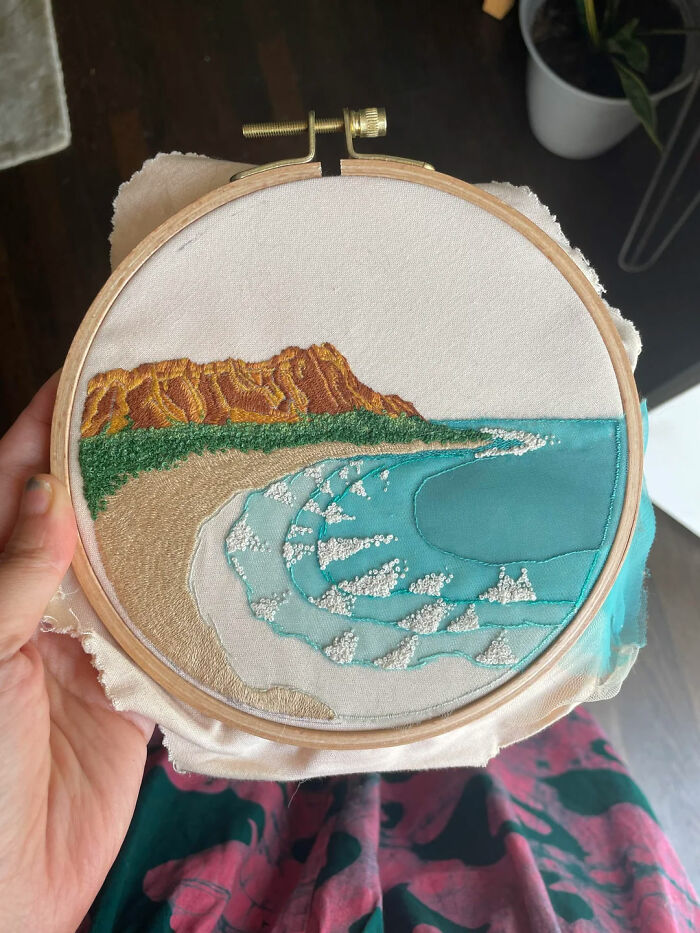 Hand holding embroidery hoop with a beautiful beach and ocean scene embroidery design in progress.