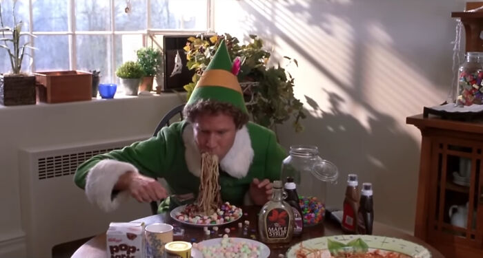 Actor in elf costume eating spaghetti with marshmallows, illustrating horrifying behind-the-scenes movie facts.