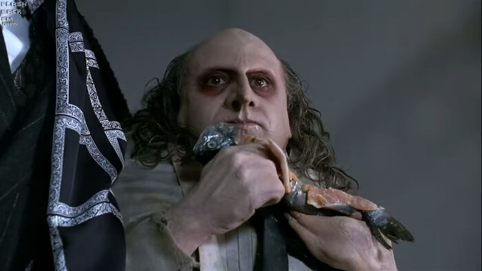 Close-up of a creepy character in makeup holding a fish, depicting a horrifying behind-the-scenes movie moment.