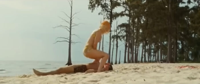 Actors performing a beach scene with one person lying down and another crouching during behind the scenes filming facts from movies.