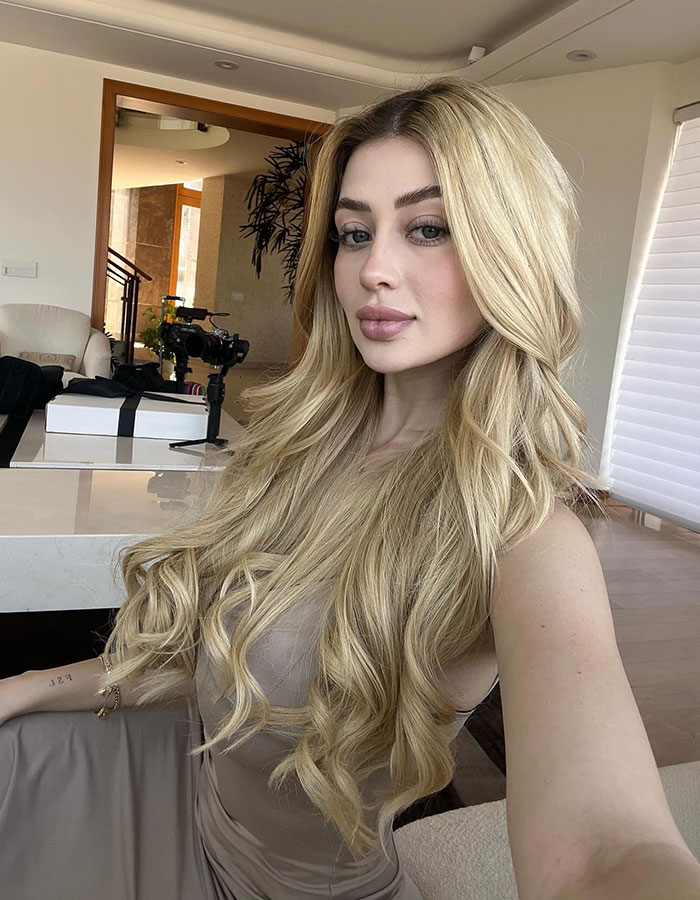 Beauty influencer with long blonde hair taking a selfie indoors amid major update in hitman ex suspect case.