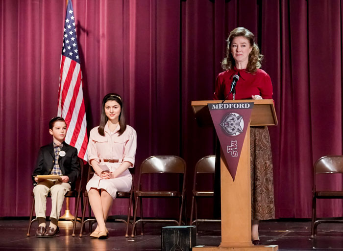 Actress from Desperate Housewives and Young Sheldon speaking at a podium on stage with two seated children nearby.