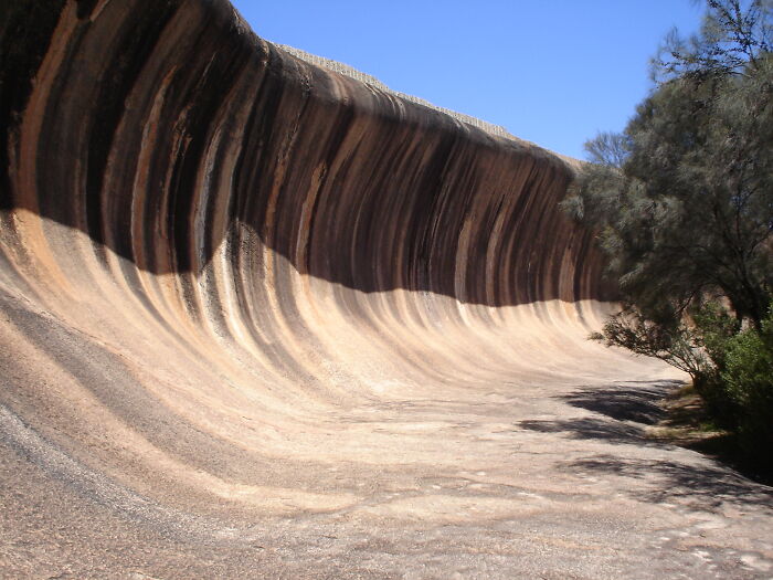 Curved rock formation with striped patterns under a clear blue sky, capturing rare natural phenomena in a desert setting.