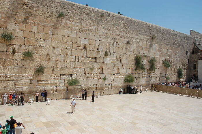Visitors gathered at the ancient UNESCO treasure site, a historic stone wall under a clear blue sky.