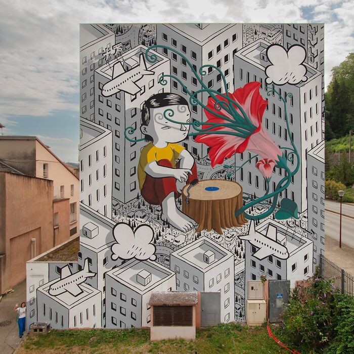 Mural by Italian artist transforming city walls into whimsical worlds with cartoon-style buildings and vibrant floral elements.