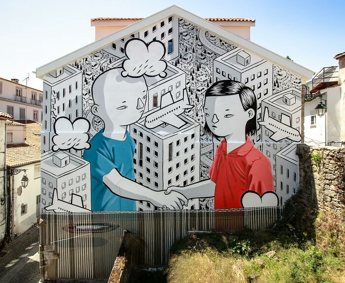 Mural by Italian artist on city wall showing two whimsical characters shaking hands against a detailed urban backdrop.