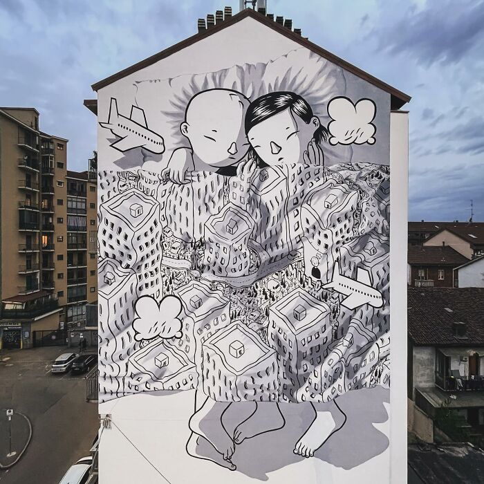 Mural by Italian artist depicting whimsical cityscape with two figures, planes, and clouds on a large city wall.