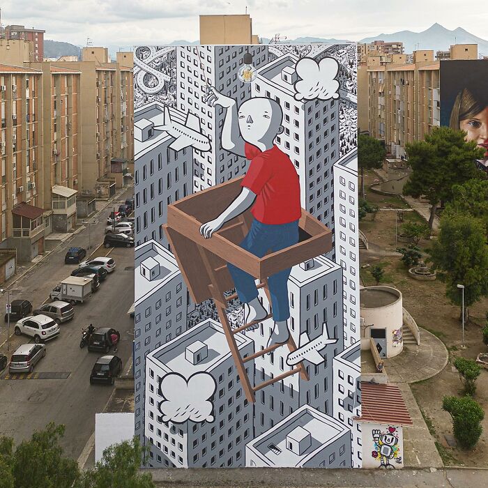 Large mural by Italian artist shows a whimsical character climbing a ladder among city buildings on an urban wall.
