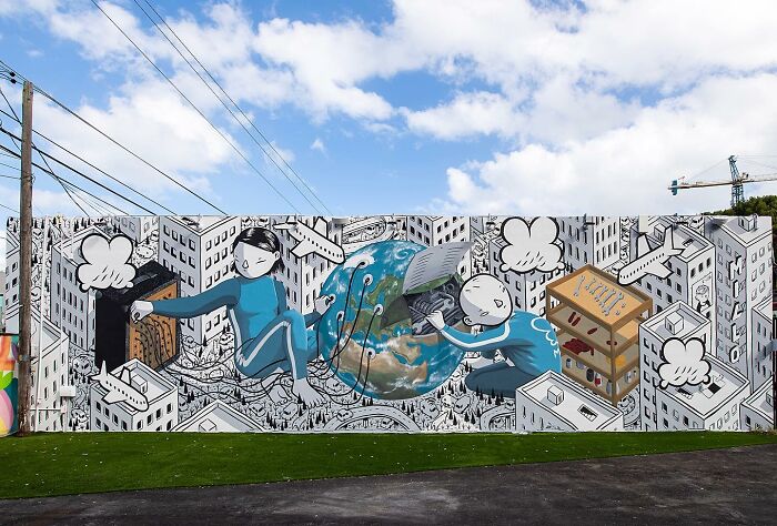 Mural by Italian artist featuring whimsical cityscape, two figures interacting with a globe and urban elements on a wall.
