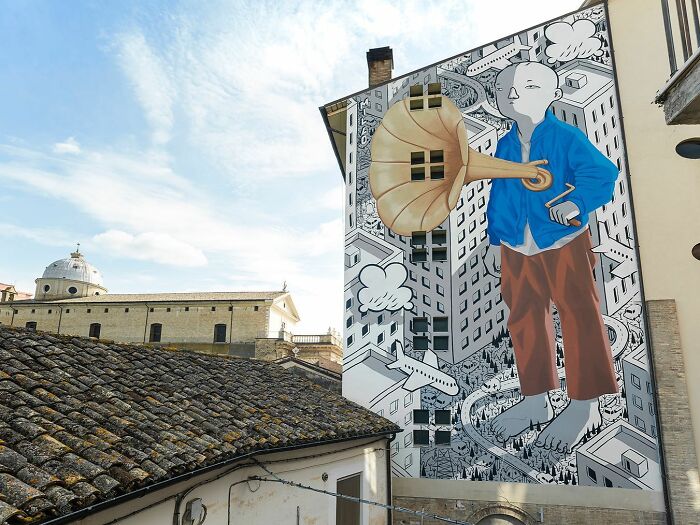 Large mural by Italian artist on city wall depicting a whimsical character with a gramophone in an urban setting.