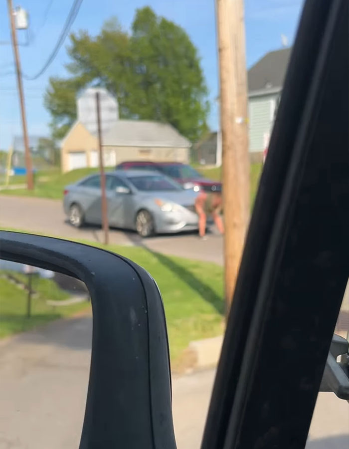 Road-raged woman crouching near a car on a suburban street, capturing a viral poopetrator incident.