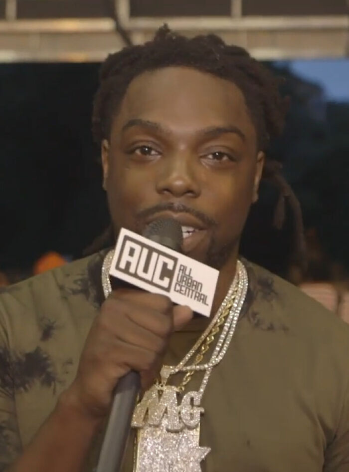 Man holding microphone with All Urban Central logo, representing notable people who passed away in 2025 in an interview setting.