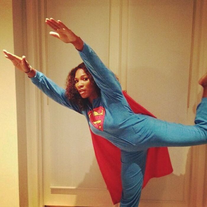 Celebrity Instagram post showing a woman in a superhero costume posing indoors with arms extended in a flying stance.