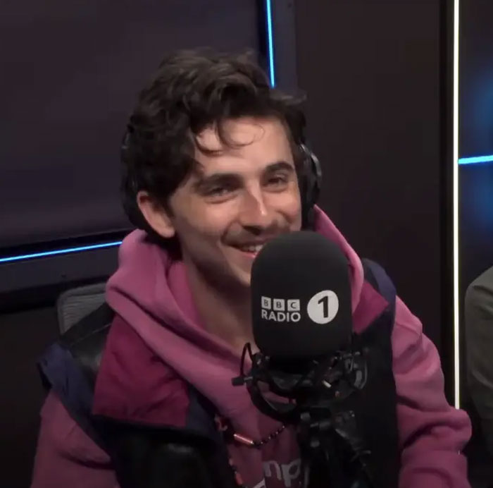 Young man wearing headphones and a pink hoodie smiling during a BBC Radio 1 interview about celebrity hygiene habits.