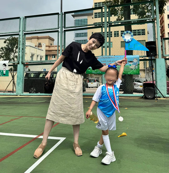 Mother and child at preschool event on outdoor court, child wearing sports medal and holding a blue flag. Mother and child at preschool event on outdoor court, child wearing sports medal and holding a blue flag.