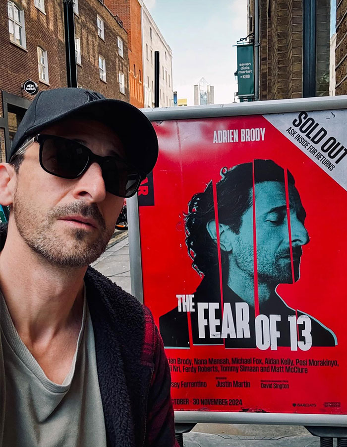 Adrien Brody wearing sunglasses and a cap, standing next to a promotional poster for The Fear of 13 artwork. Adrien Brody wearing sunglasses and a cap, standing next to a promotional poster for The Fear of 13 artwork.