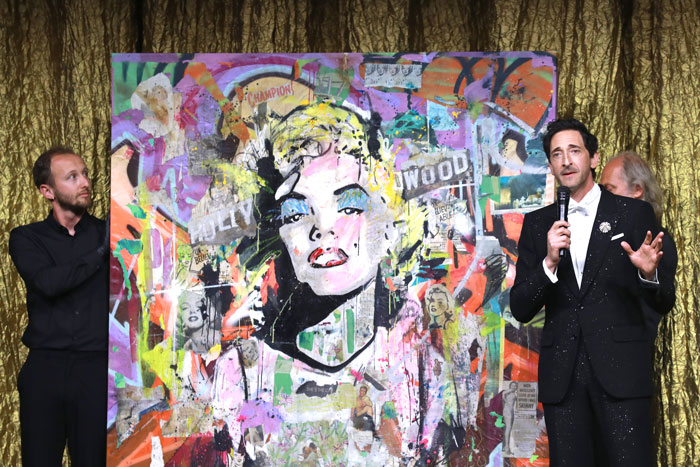 Adrien Brody unveiling a colorful mixed media art piece at Cannes while people react and comment on his artwork. Adrien Brody unveiling a colorful mixed media art piece at Cannes while people react and comment on his artwork.
