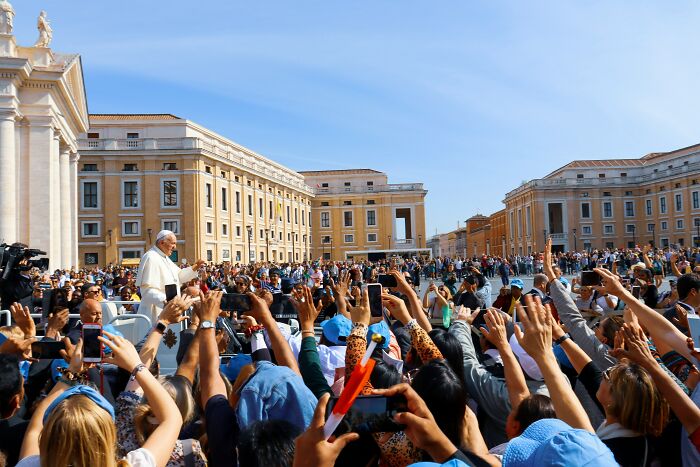 Large crowd at a historic event raising hands and capturing moments on phones during a bizarre historical moment outdoors.