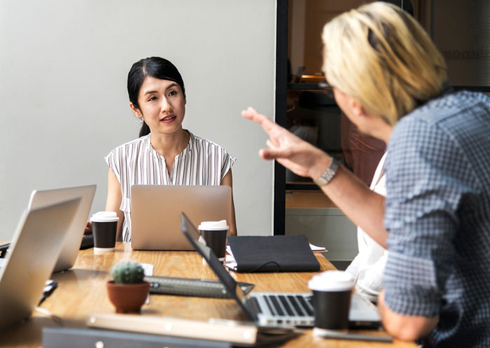 Two coworkers discussing creative ideas over laptops in a meeting, highlighting graphic designer&rsquo;s work conflict.