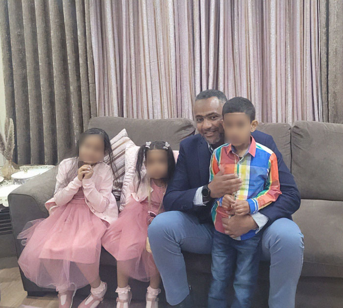 Father of four with few followers sitting on a couch with children, smiling in a home living room setting.