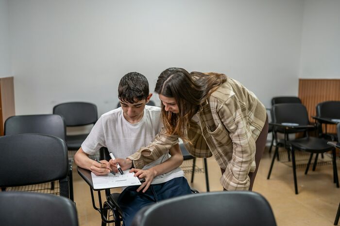 Teacher helping a student with classwork in an empty classroom, demonstrating unhinged but effective teaching methods.