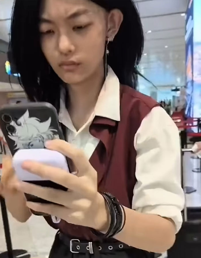 Young passenger at airport checking phone after facial recognition failed, asked to remove makeup during security process