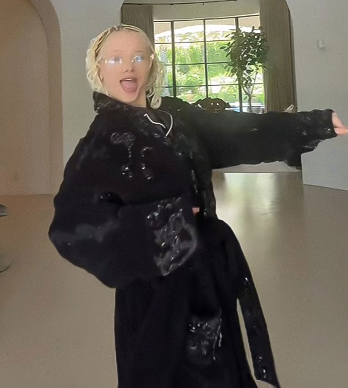 Alabama Barker smiling and posing indoors wearing a black outfit with glasses and blonde hair styled in waves. Alabama Barker smiling and posing indoors wearing a black outfit with glasses and blonde hair styled in waves.