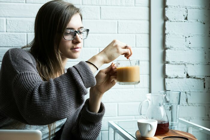 Woman in glasses stirring coffee, representing discussion on jobs that shouldn’t be earning as much as they do online