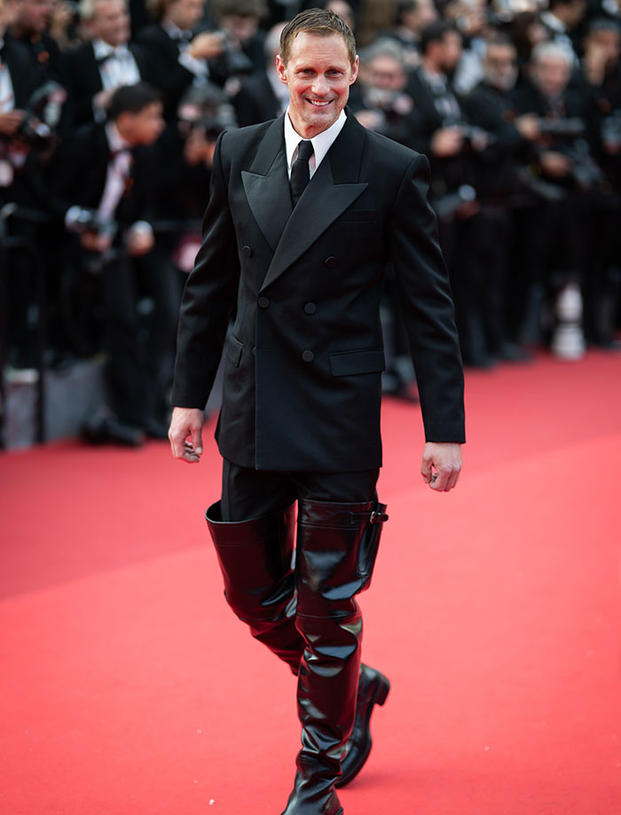 Actor on red carpet wearing black suit and leather thigh-high boots at event linked to Harry Potter star in X-rated gay film.