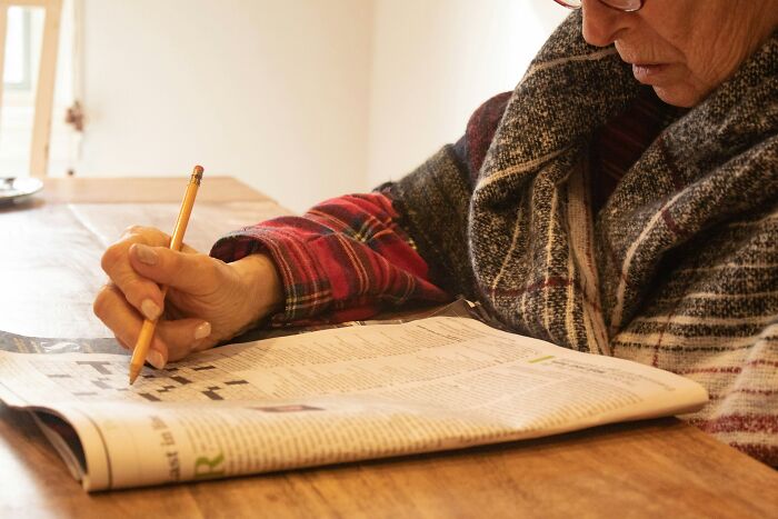 Person in a patterned sweater solving a crossword puzzle in a newspaper, illustrating bizarre historical events concept.