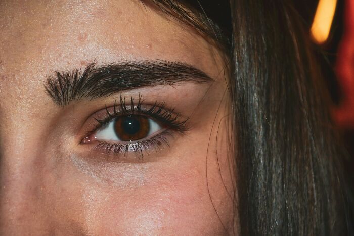 Close-up of a woman's eye and eyebrow, focusing on natural skin texture and dark brown eye detail.
