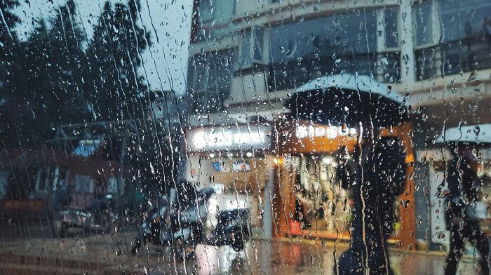 Raindrops on a window with a blurred view of a person holding an umbrella, illustrating low-key pleasures of simple moments.