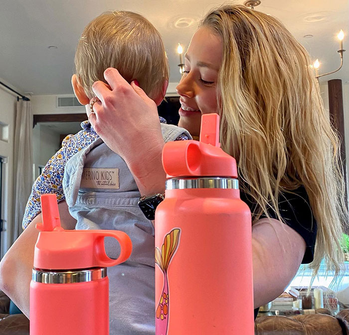 Amber Heard holding her child at home with pink water bottles in the foreground relating to potty training. Amber Heard holding her child at home with pink water bottles in the foreground relating to potty training.