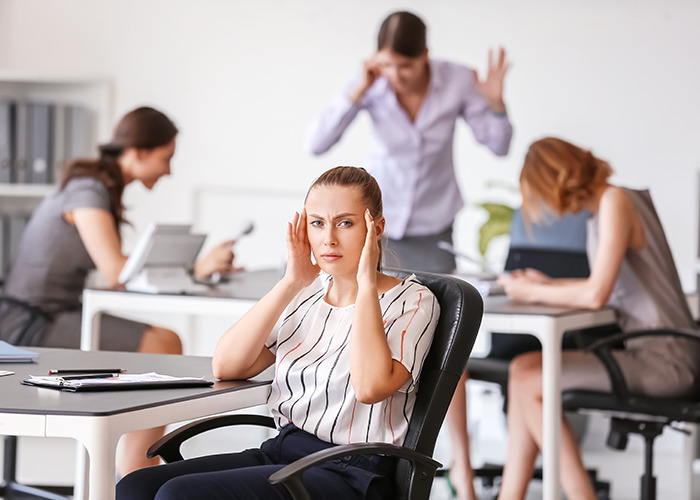 American woman in office appearing stressed while British colleagues discuss her usual US habits seen as rude.
