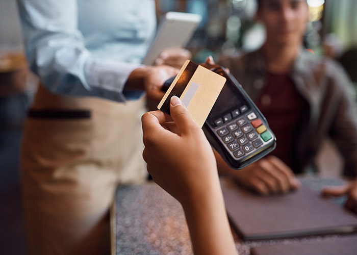 American woman staying in UK paying with card at restaurant while British staff holds a payment terminal.