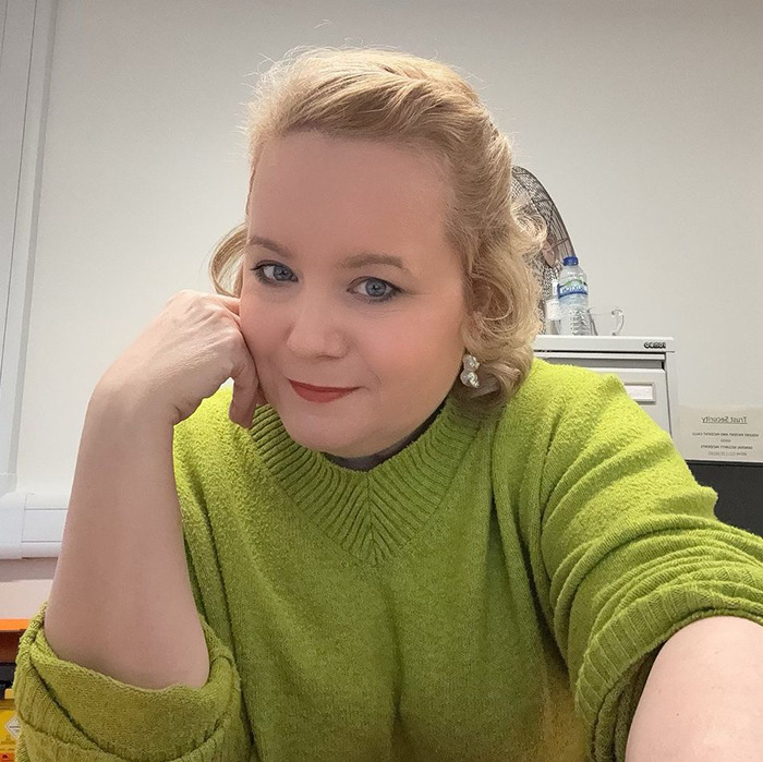 American woman in a green sweater staying in UK reflecting on cultural differences and US habits considered rude.