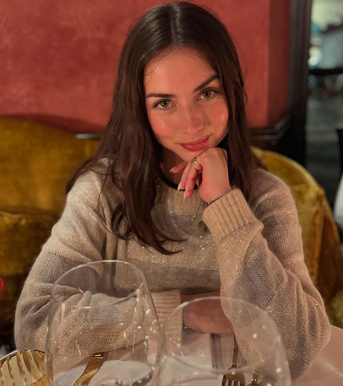 Ana De Armas wearing a beige sweater, smiling subtly while seated at a table during an event with Tom Cruise. Ana De Armas wearing a beige sweater, smiling subtly while seated at a table during an event with Tom Cruise.
