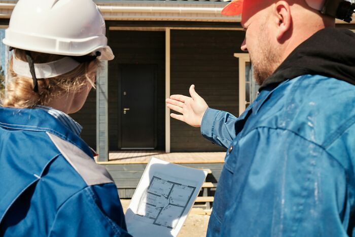 Two construction workers in helmets reviewing building plans, discussing job site details related to jobs earning income.