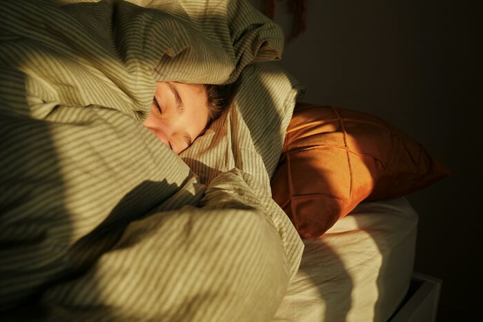 Person wrapped in a blanket sleeping peacefully in bed, illustrating excessive laziness shared by 43 people.