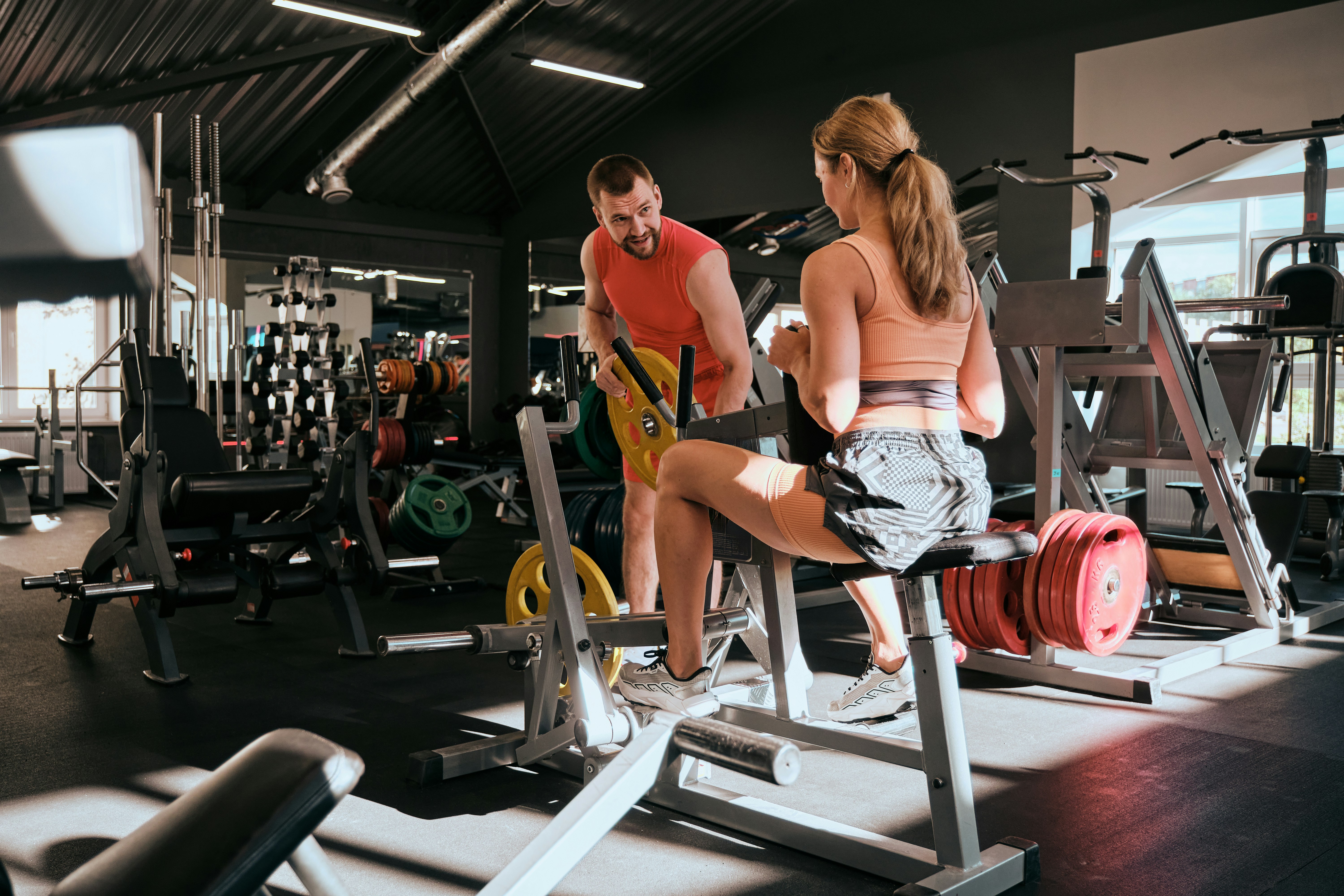 Man and woman in gym engaging in awkward gym flirting with weights and fitness machines around them.