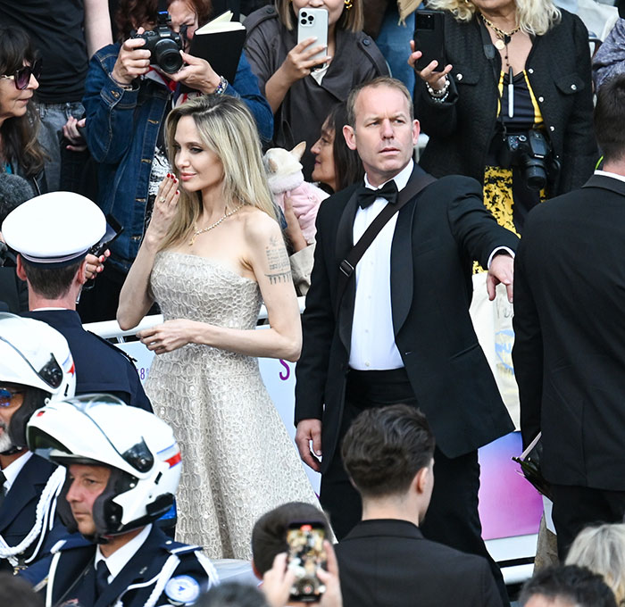 Angelina Jolie at an event appearing uncomfortable with her bodyguard while surrounded by a crowd and photographers.