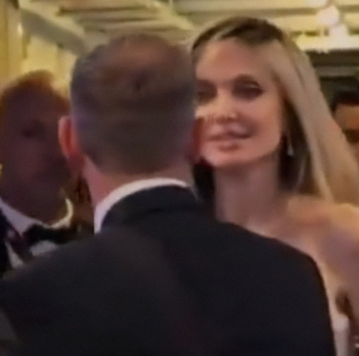 Angelina Jolie appearing uncomfortable in a crowded event with her bodyguard close by, low lighting setting.